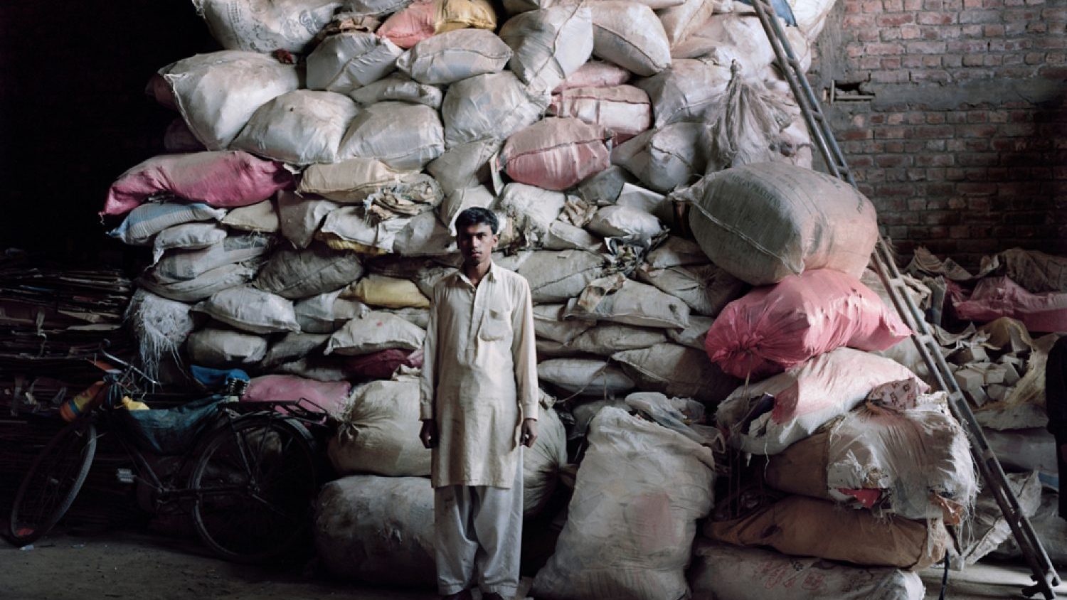 Valentino Bellini. Lahore, Pakistan. A guy stands in front of a huge pile of electronic components which will later be processed to extract precious metals.